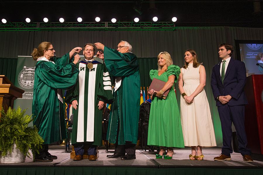 Northwest Regents Mel Tjeerdsma 和 Roxanna Swaney placed the University's chain of office on Dr. 兰斯·塔图姆的肩膀，他的家人在一旁看着. (Photo by Lauren Adams/<a href='http://xzitnt.modonexpress.net'>威尼斯人在线</a>)